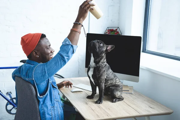 Bonito homem afro-americano brincando com o cão na mesa de computador — Fotografia de Stock