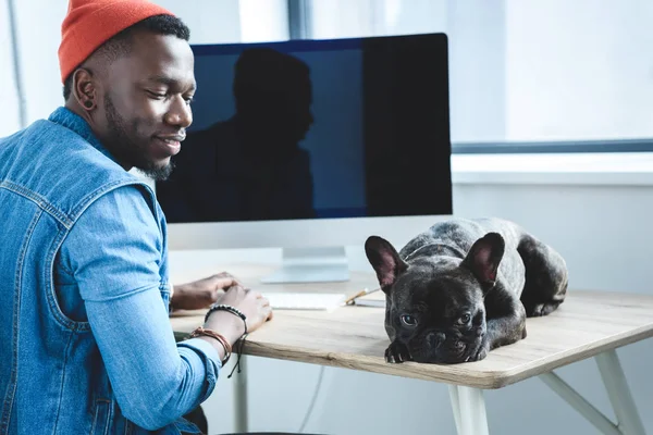 Aburrido perro esperando a que el hombre afroamericano termine el trabajo por computadora - foto de stock