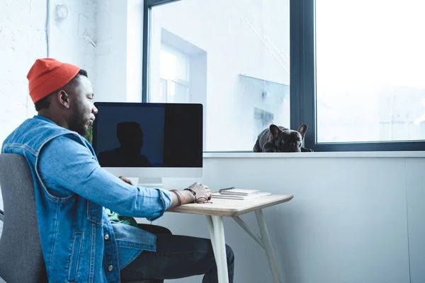 Young man working by computer while Frenchie dog lying on windowsill — Stock Photo