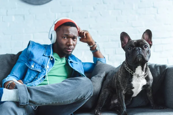 Young man in headphones listening to music and sitting by French bulldog — Stock Photo