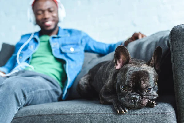 Africano americano em fones de ouvido ouvir música e sentado por bulldog francês — Fotografia de Stock