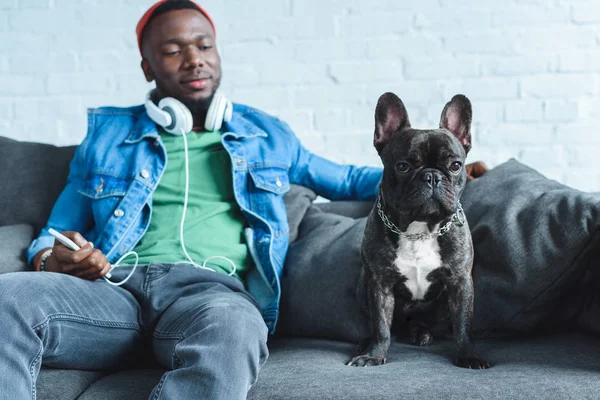 Young man in headphones holding smartphone and sitting by French bulldog — Stock Photo