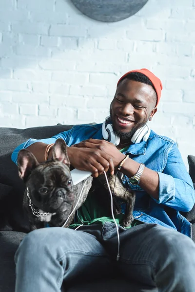 Africano americano em fones de ouvido abraçando bulldog francês — Fotografia de Stock