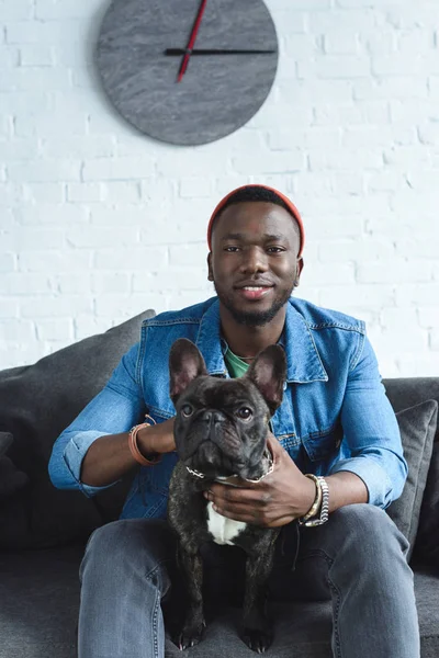 Junger Mann mit französischer Bulldogge sitzt auf Sofa — Stockfoto