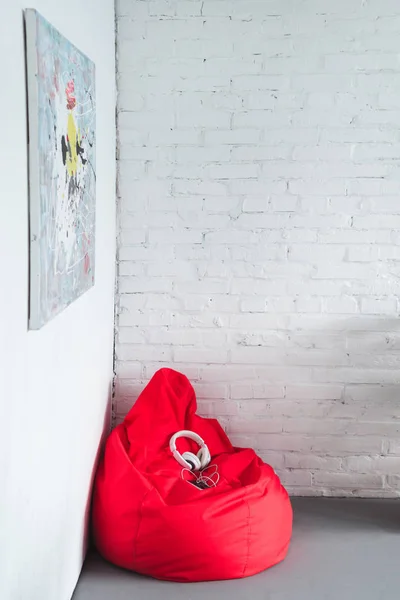 Smartphone avec casque sur sac haricot rouge par mur blanc — Photo de stock