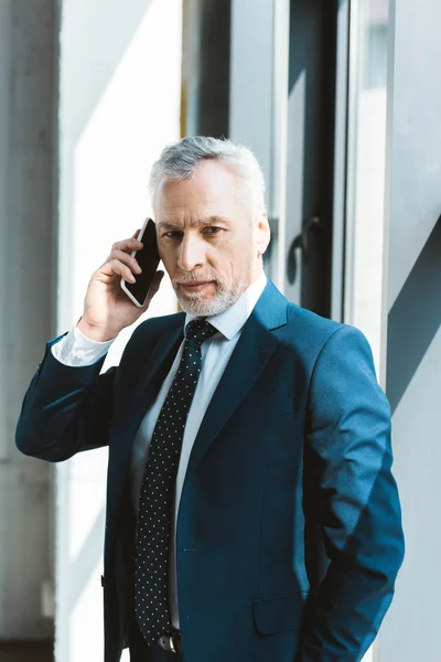 Serio hombre de negocios senior hablando por teléfono inteligente y mirando a la cámara - foto de stock