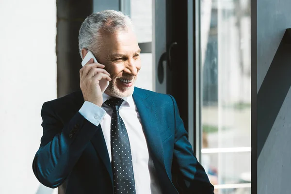 Allegro uomo d'affari anziano che parla da smartphone e guarda la finestra — Foto stock