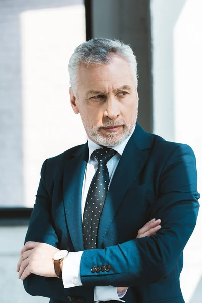 Retrato de un hombre de negocios de confianza de pie con los brazos cruzados y mirando hacia otro lado - foto de stock