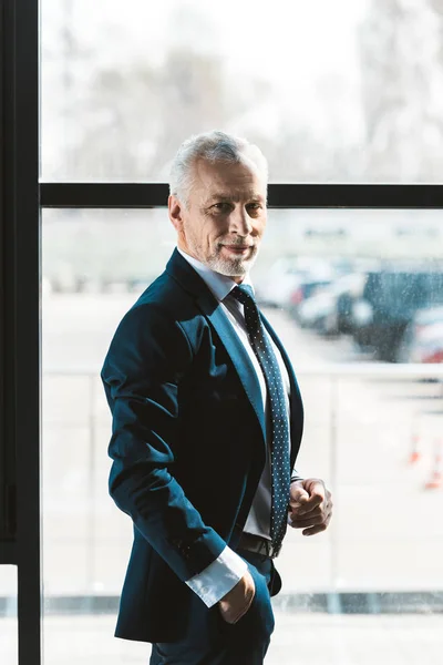 Retrato de hombre de negocios alto guapo de pie con la mano en el bolsillo y sonriendo a la cámara - foto de stock