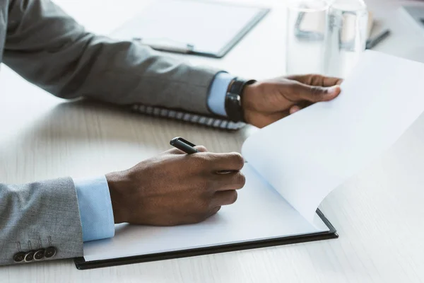 Cropped shot of african american businessman writing on blank clipboard — Stock Photo