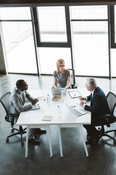 Vista de ángulo alto de la gente de negocios multiétnicos profesionales trabajando juntos en la mesa en la oficina moderna - foto de stock