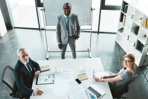 Hochwinkelaufnahme von professionellen multiethnischen Geschäftsleuten, die während eines Meetings im Büro in die Kamera lächeln — Stock Photo