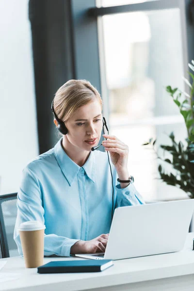 Donna d'affari in auricolare utilizzando il computer portatile in ufficio — Foto stock