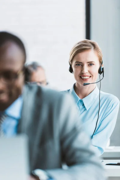 Selektiver Fokus der schönen Geschäftsfrau im Headset, die in die Kamera lächelt — Stockfoto