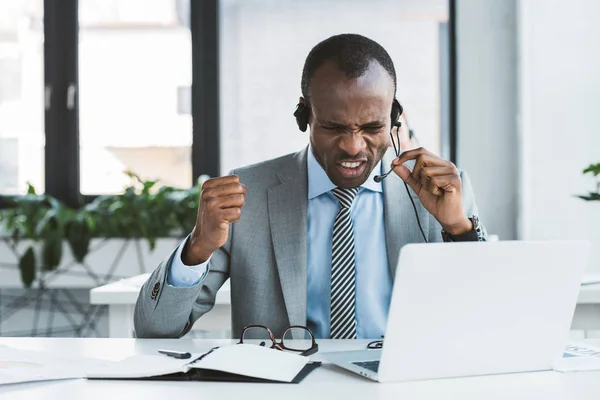 Emotional african american businessman yelling at headset at workplace — Stock Photo