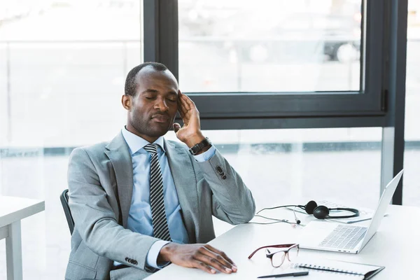 Joven hombre de negocios afroamericano que sufre de dolor de cabeza mientras está sentado en el lugar de trabajo - foto de stock