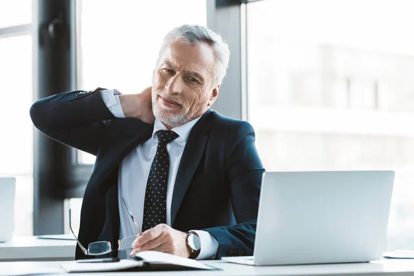 Senior businessman suffering from pain in neck while working with laptop — Stock Photo