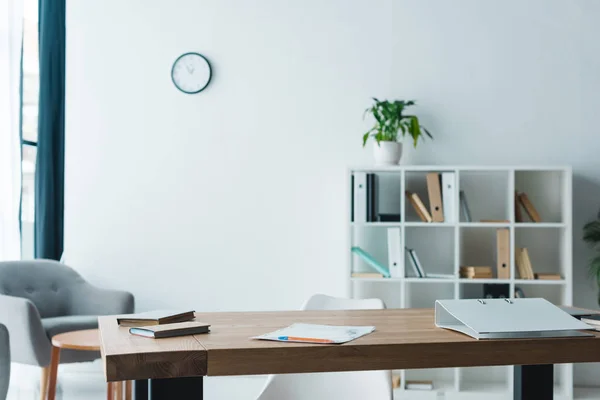 Table en bois avec dossier, livres et papiers dans un bureau moderne — Photo de stock