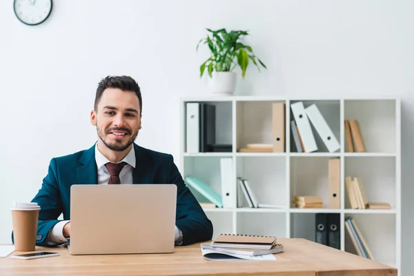 Schöner lächelnder junger Geschäftsmann mit Laptop am Arbeitsplatz — Stockfoto