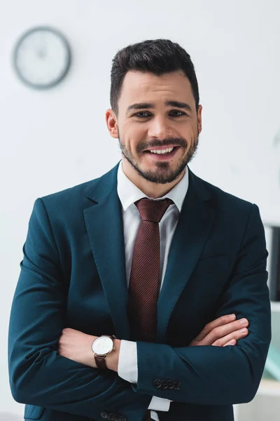 Portrait of handsome young businessman with crossed arms smiling at camera — Stock Photo