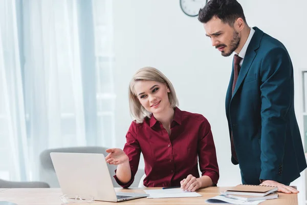 Smiling young business people working together and looking at laptop in office — Stock Photo