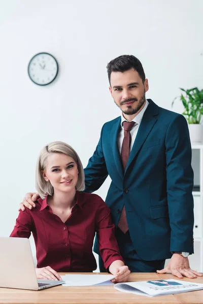 Schöne junge Geschäftsleute lächeln in die Kamera, während sie gemeinsam im Büro arbeiten — Stockfoto