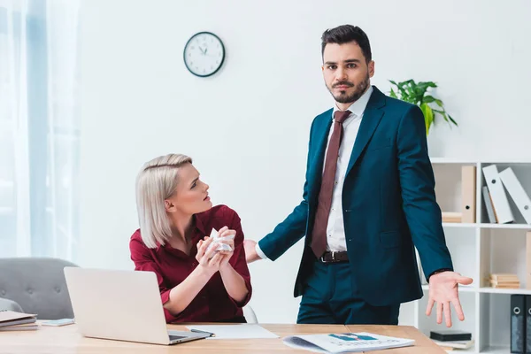 Junge Geschäftsfrau hält zerknülltes Papier in der Hand und blickt auf männlichen Amtskollegen — Stockfoto