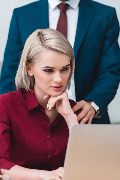 Cropped shot of businessman flirting with beautiful young businesswoman using laptop at workplace — Stock Photo