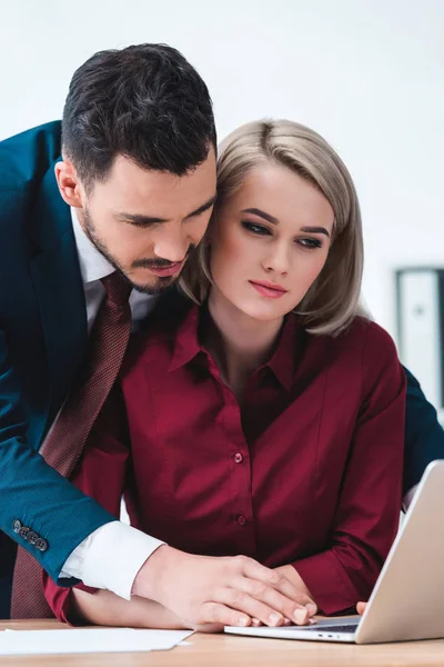 Handsome businessman flirting with beautiful female colleague using laptop in office — Stock Photo
