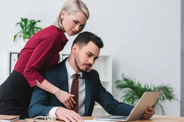 Young business colleagues using laptop and flirting in office — Stock Photo