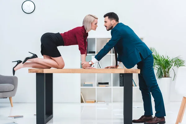 Side view of seductive young couple looking at each other while flirting in office — Stock Photo