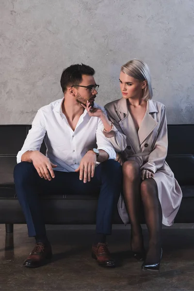 Sexy giovane donna in cappotto e calze flirtare con bello giovane uomo d'affari seduto sul divano — Foto stock