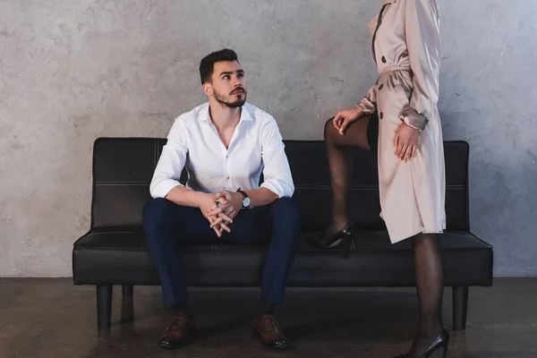 Cropped shot of businessman sitting on couch and looking at sexy girl in coat and stockings — Stock Photo