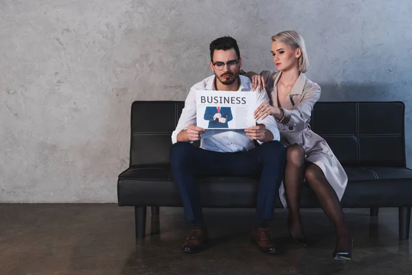 Сексуальная девушка в чулках флиртует с привлекательным бизнесменом читающим газету на диване — стоковое фото