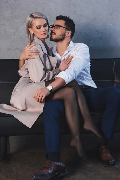 Schönes verführerisches junges Paar, das sich auf dem Sofa im Büro umarmt — Stockfoto