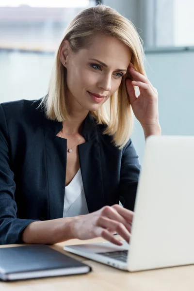 Sonriente rubia mujer de negocios usando portátil en el lugar de trabajo - foto de stock