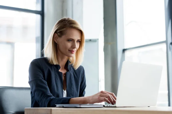 Donna d'affari professionale sorridente che lavora con computer portatile in ufficio — Foto stock