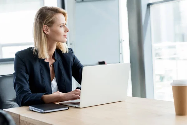 Pensive buisnesswoman looking away while using laptop at workplace — Stock Photo