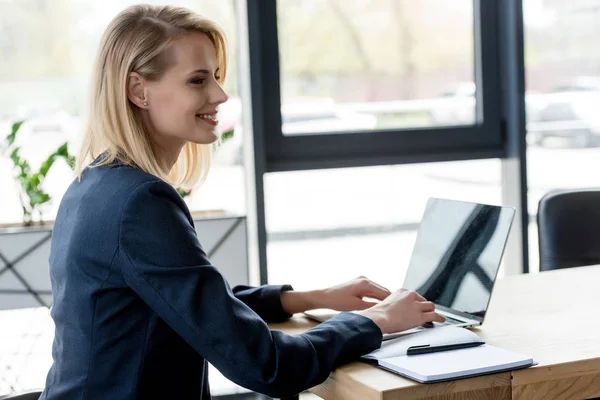 Привлекательная улыбающаяся деловая женщина с ноутбуком на рабочем месте — стоковое фото