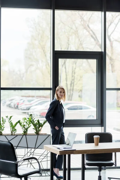 Уверенная деловая женщина смотрит в камеру, стоя в современном офисе — стоковое фото