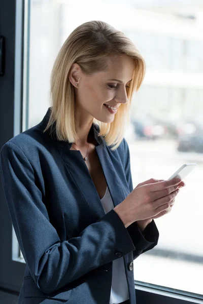 Lächelnde Geschäftsfrau in offizieller Kleidung mit Smartphone — Stockfoto