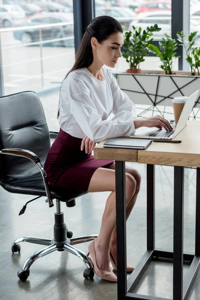 Hermosa joven mujer de negocios utilizando el ordenador portátil en el lugar de trabajo - foto de stock