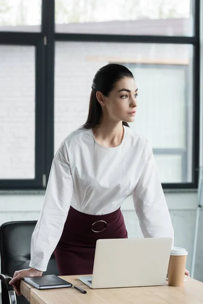 Beautiful young businesswoman leaning at table and looking away in office — Stock Photo