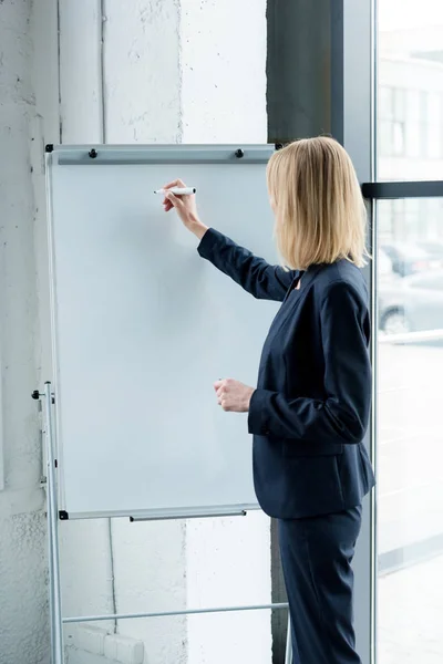 Seitenansicht einer professionellen Geschäftsfrau, die auf einem leeren Whiteboard im Büro schreibt — Stockfoto