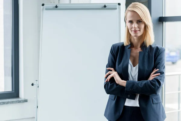 Красивая уверенная деловая женщина, стоящая со скрещенными руками и улыбающаяся в офисе перед камерой — стоковое фото