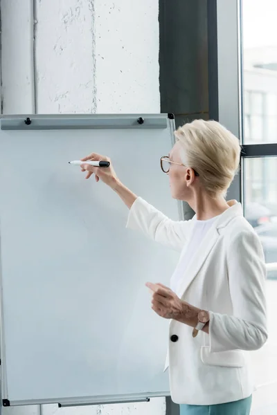 Professional businesswoman in eyeglasses writing on whiteboard in office — Stock Photo