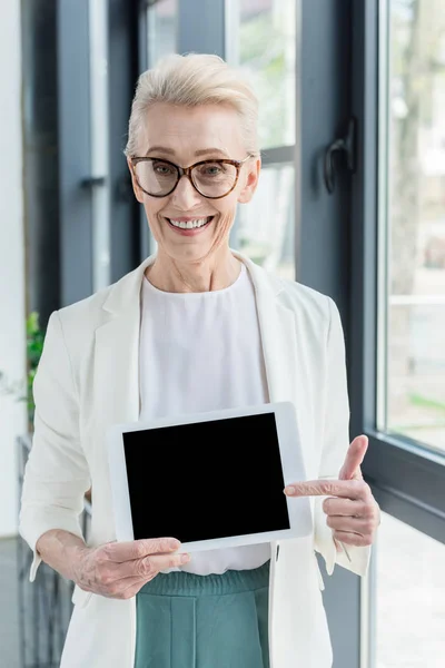 Бізнес-леді в окулярах тримає цифровий планшет з порожнім екраном і посміхається на камеру — стокове фото