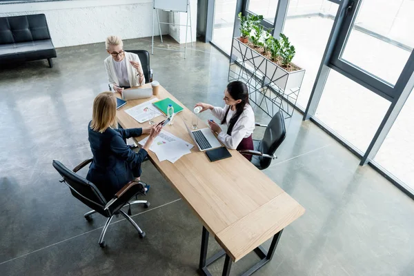 Vista de ángulo alto de tres empresarias profesionales que trabajan con gadgets y papeles en la oficina - foto de stock