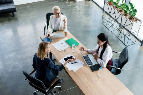 Visão de alto ângulo de três empresárias profissionais discutindo projeto no local de trabalho — Fotografia de Stock