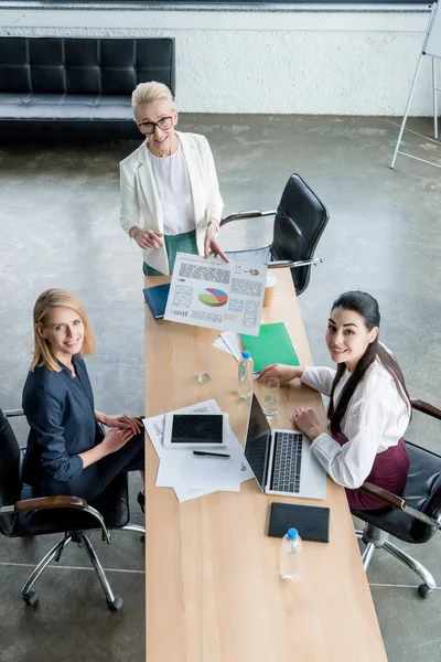 Visão de alto ângulo das empresárias sorrindo para a câmera enquanto trabalham juntas no escritório — Fotografia de Stock